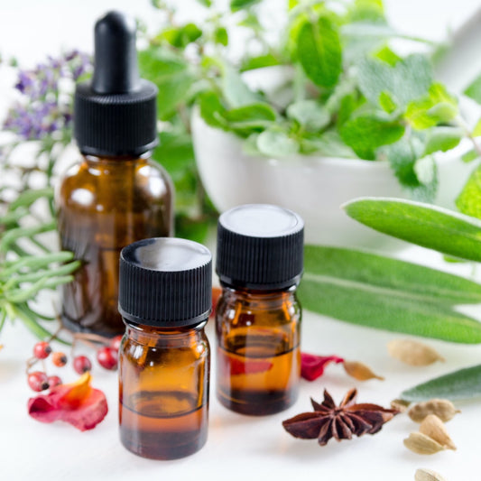 Three brown bottles of essential oils surrounded by herbs used in aromatherapy services